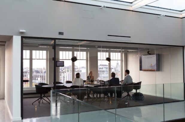 Four people sitting at a conference table in an all-glass meeting room discussing strategic account planning.